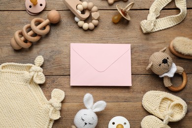 Photo of Baby shower party. Envelope surrounded by stuff for child on wooden background, flat lay