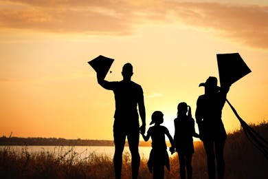 Image of Silhouette of family with kites near river at sunset