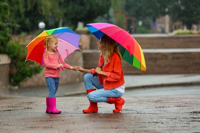 Happy mother and daughter with bright umbrella under rain outdoors