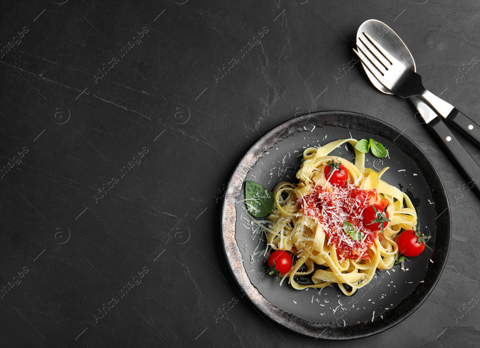 Photo of Tasty pasta and cutlery on black table, flat lay. Space for text