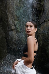 Photo of Beautiful young woman in stylish bikini near waterfall outdoors