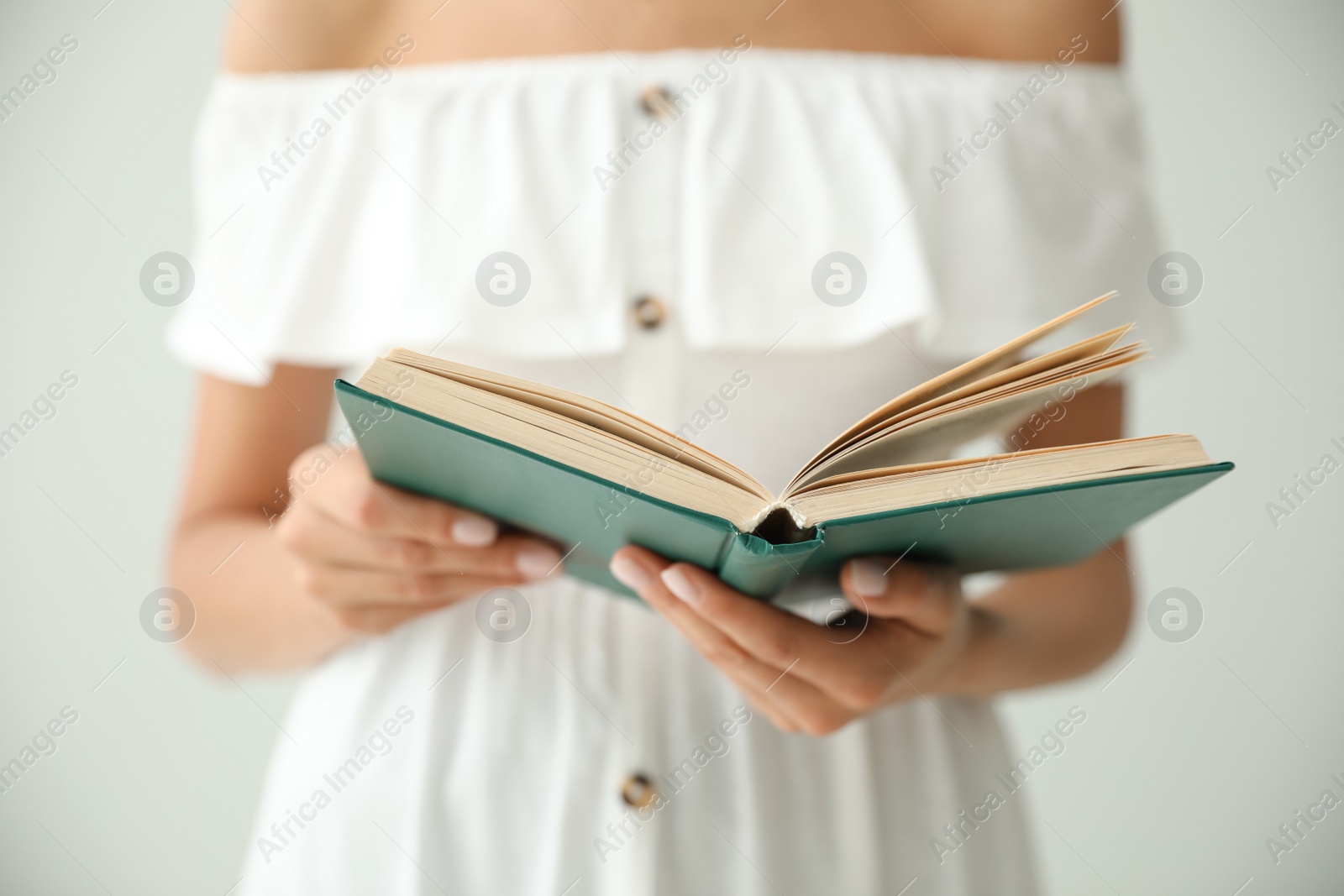 Photo of Young woman reading book on light grey background, closeup