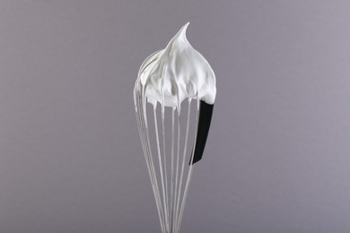 Photo of Whisk with whipped cream on grey background