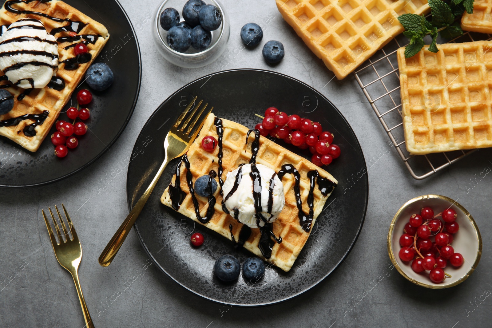 Photo of Delicious Belgian waffles with ice cream, berries and chocolate sauce on grey table, flat lay