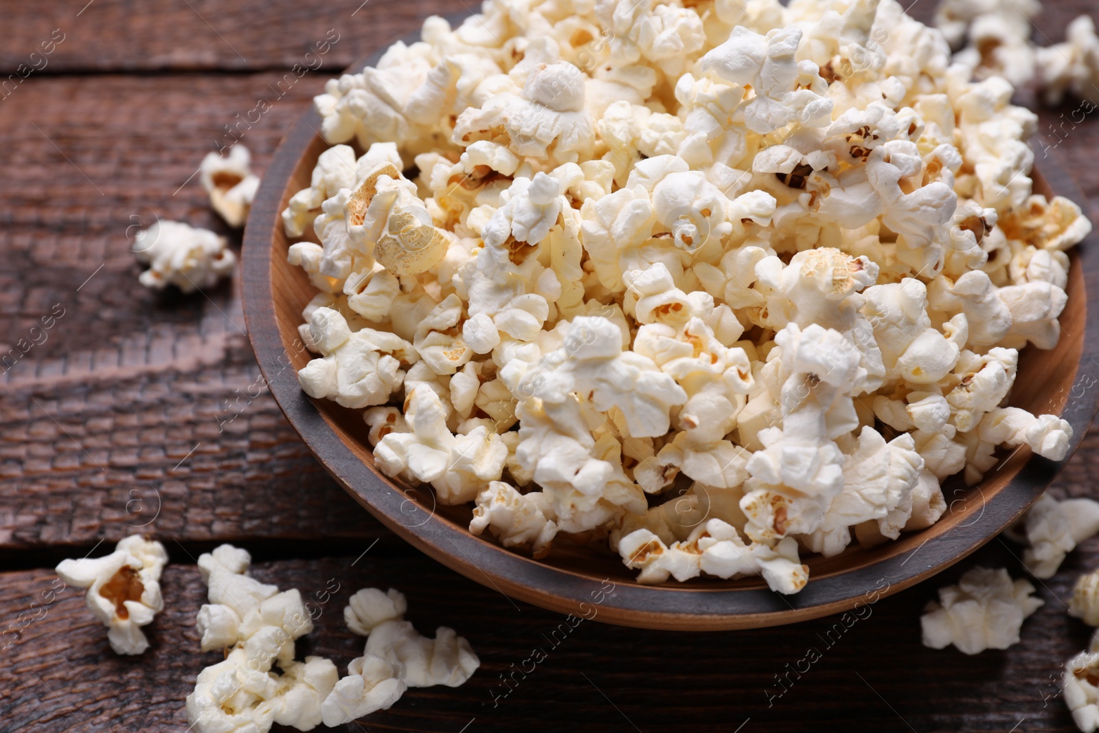 Photo of Bowl of tasty popcorn on wooden table, closeup