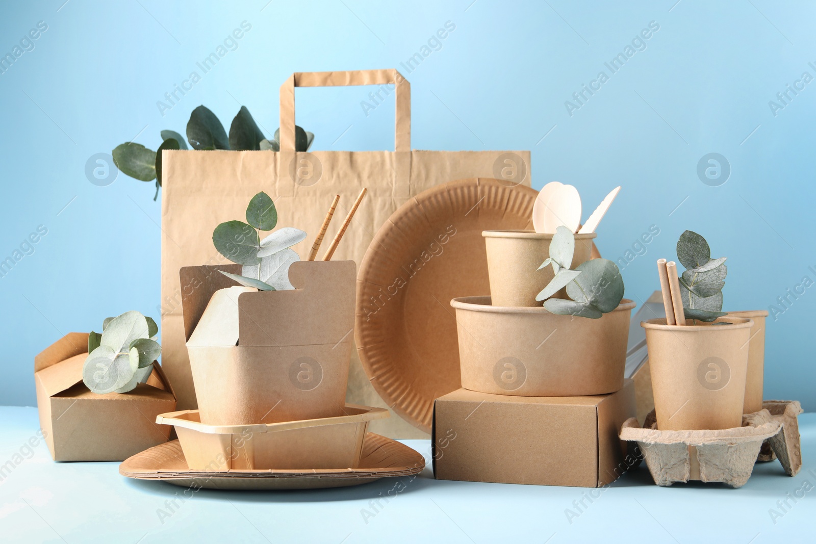 Photo of Eco friendly food packaging. Paper containers, tableware, bag and eucalyptus branches on white table against light blue background