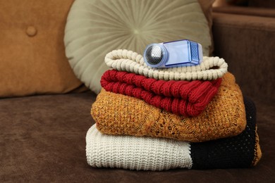 Photo of Modern fabric shaver and knitted clothes on brown sofa indoors