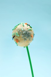 Photo of Sweet cake pop decorated with sprinkles on light blue background, closeup. Delicious confectionery