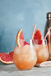 Glasses of grapefruit cocktails served on table against color background. Space for text