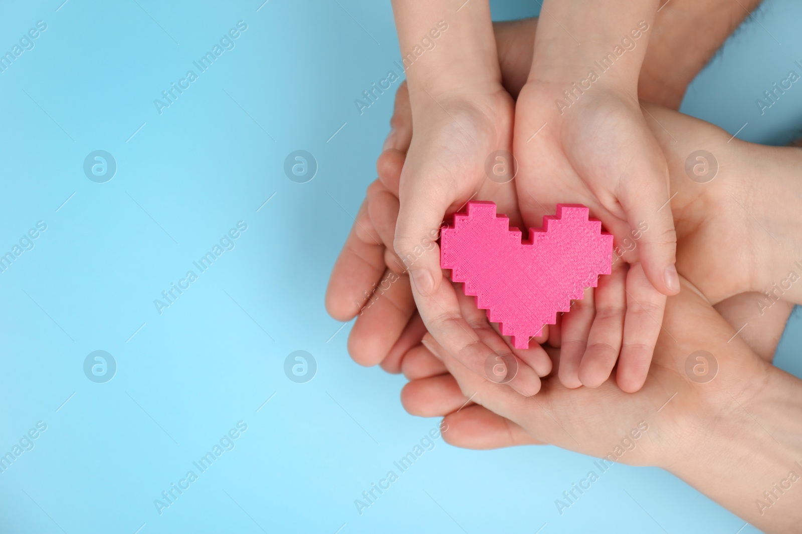 Photo of Top view of parents and kid holding pink heart in hands on turquoise background, space for text. Family day