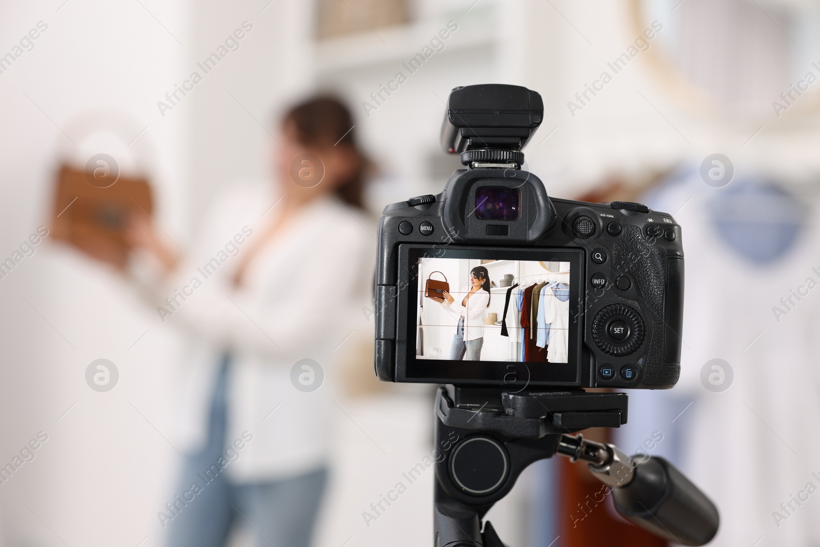 Photo of Fashion blogger showing her clothes while recording video at home, focus on camera