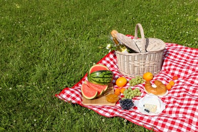 Photo of Picnic blanket with delicious food and wine outdoors on summer day, space for text