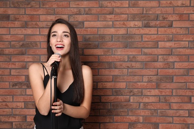 Young stylish woman singing in microphone near brick wall. Space for text