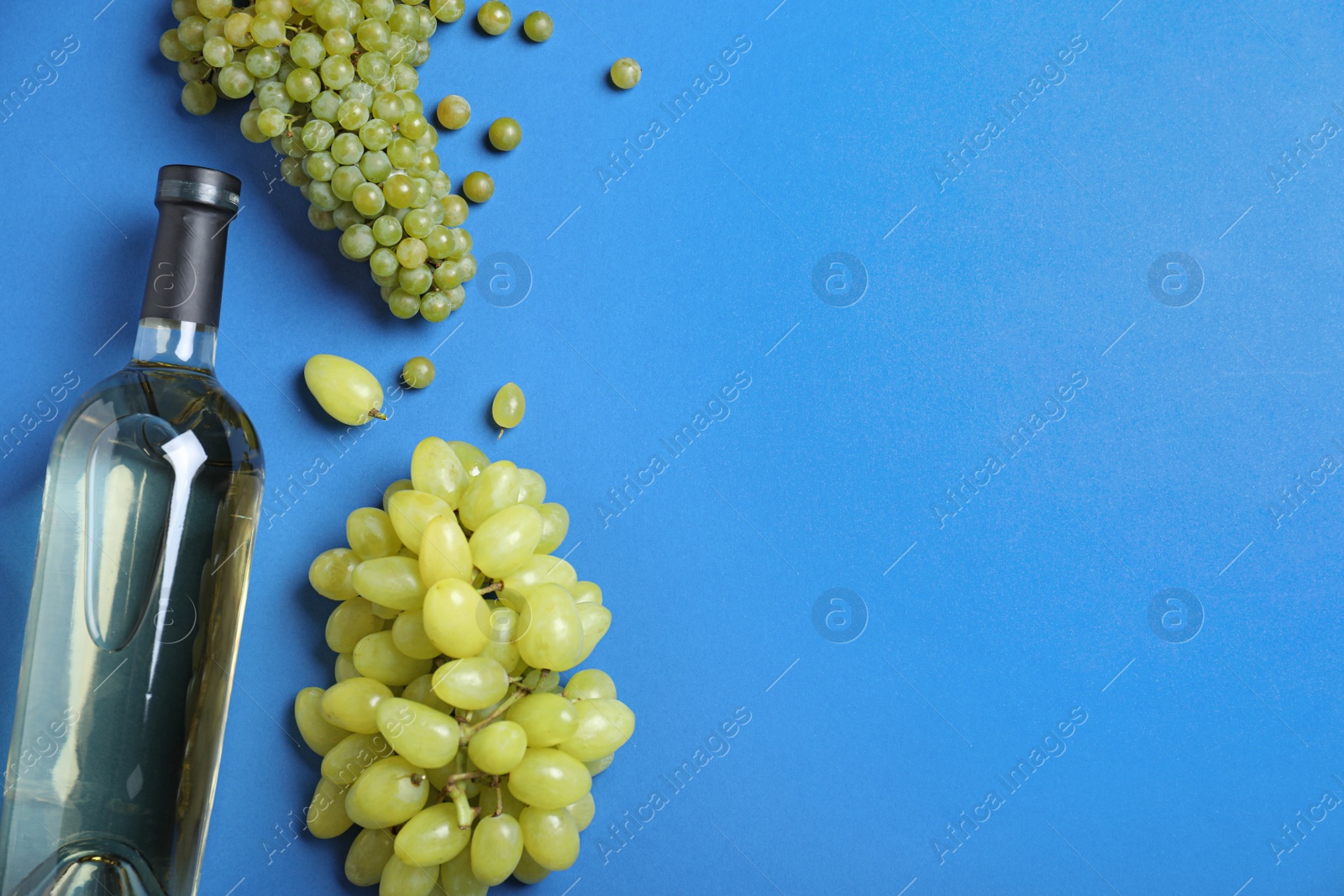 Photo of Fresh ripe juicy grapes and bottle of wine on blue background, flat lay. Space for text