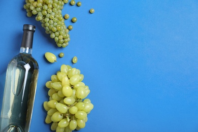 Photo of Fresh ripe juicy grapes and bottle of wine on blue background, flat lay. Space for text