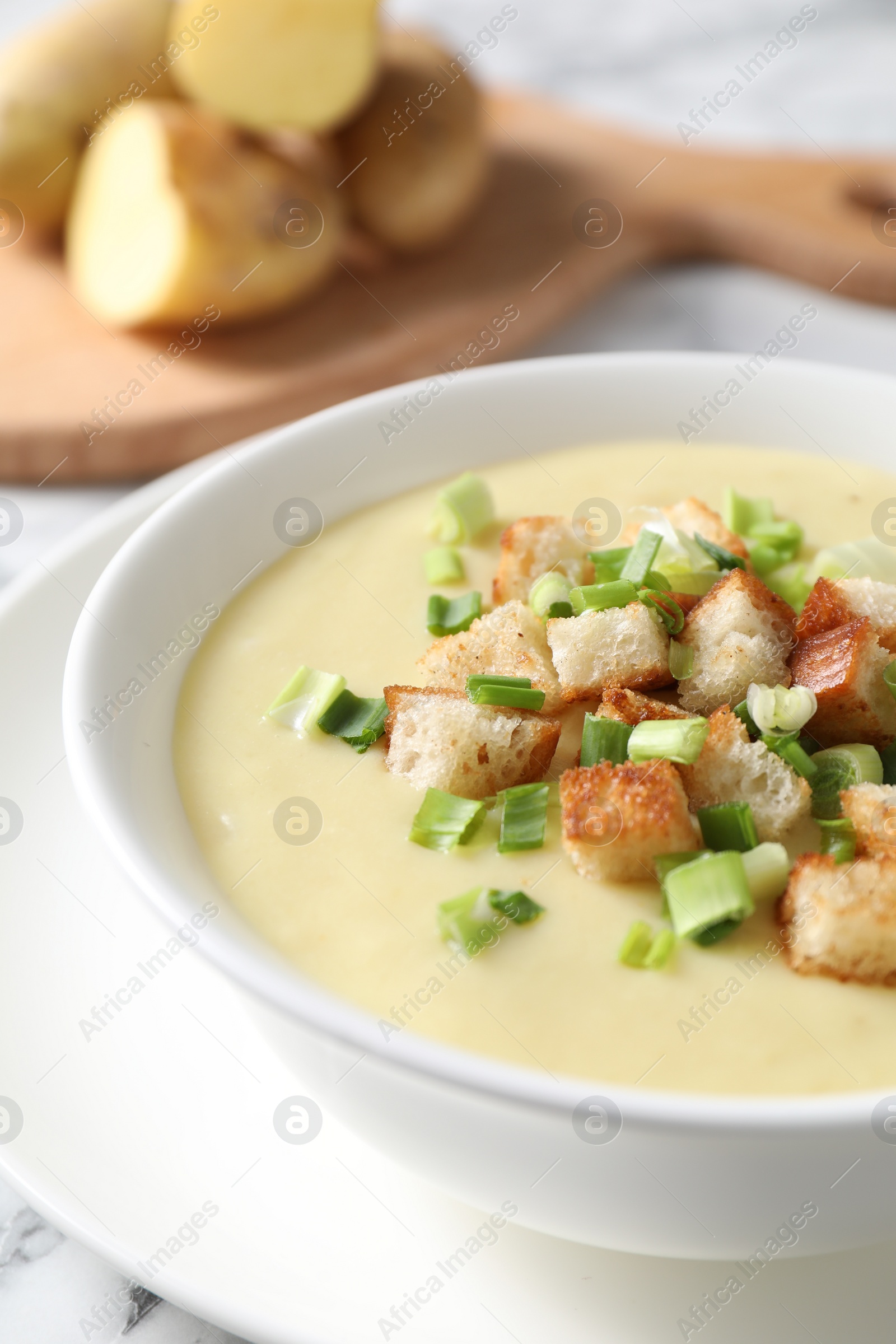 Photo of Tasty potato soup with croutons and green onion in bowl on white table, closeup