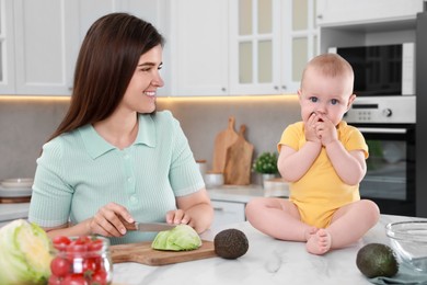Happy young woman with her cute baby spending time together in kitchen