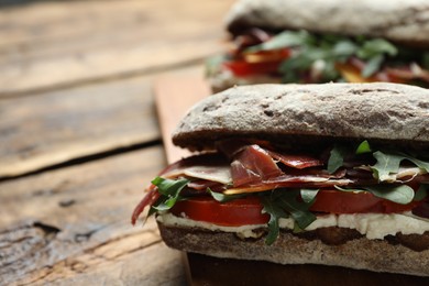 Photo of Delicious sandwiches with fresh vegetables and prosciutto on wooden table, closeup