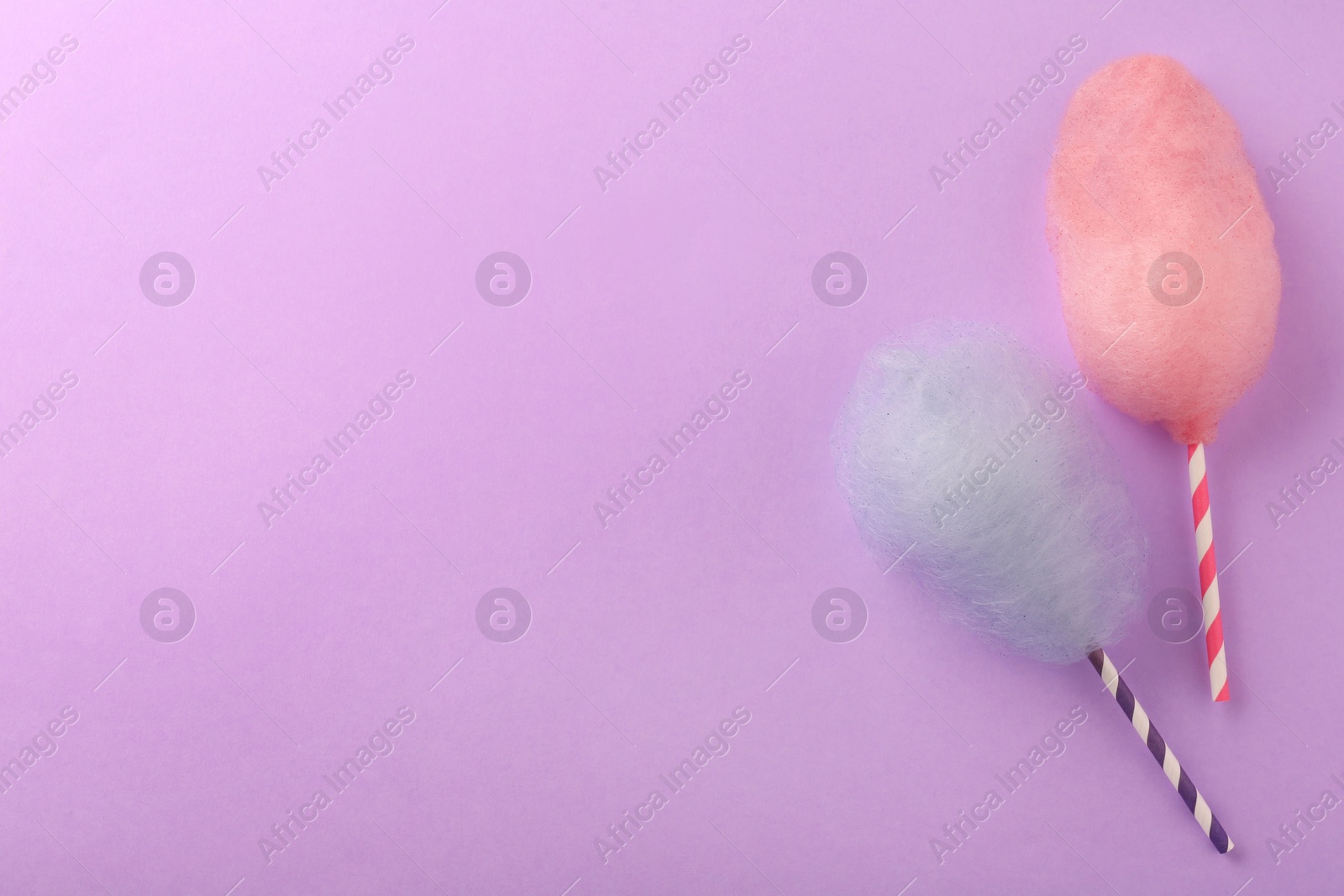 Photo of Sweet color cotton candies on violet background, flat lay. Space for text