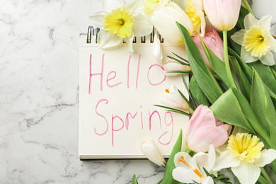 Photo of Notebook with words HELLO SPRING and fresh flowers on white marble table, flat lay