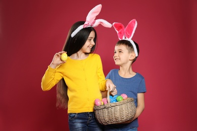 Cute children in bunny ears headbands holding basket with Easter eggs on color background