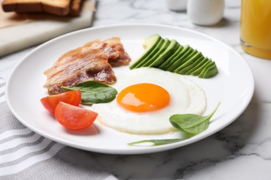 Photo of Tasty breakfast with fried egg, bacon and avocado served on white marble table, closeup