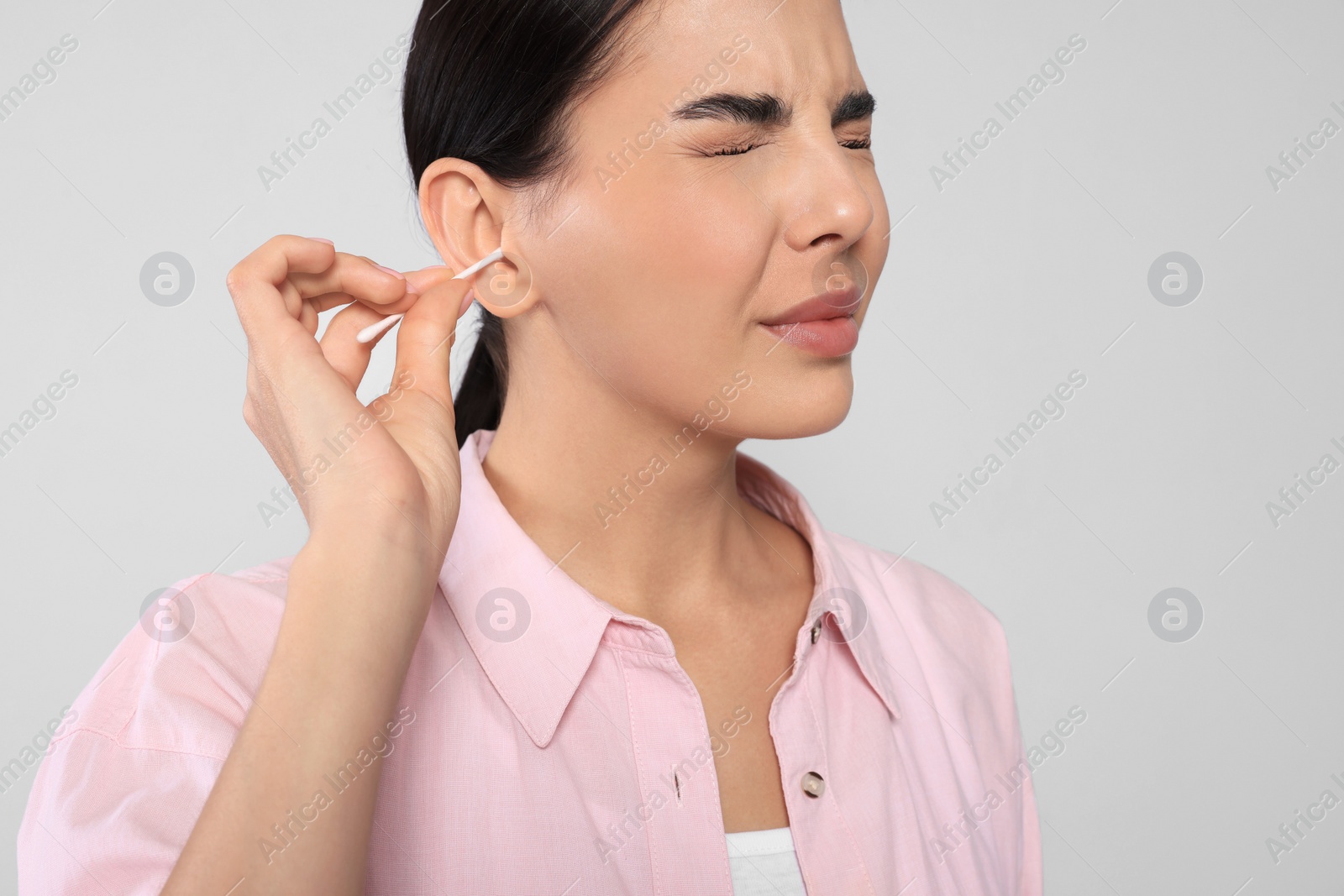 Photo of Young woman cleaning ear with cotton swab on light grey background, closeup