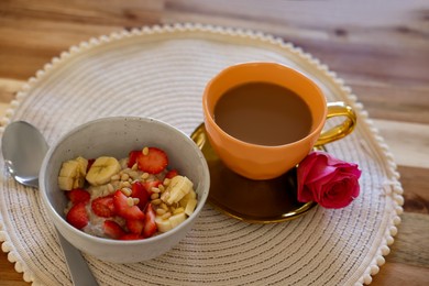 Photo of Delicious oatmeal with banana, strawberries, nuts and cup of hot drink on wooden table