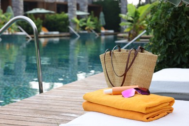 Photo of Wicker bag with beach accessories on sunbed near outdoor swimming pool, space for text. Luxury resort