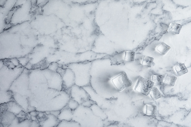 Photo of Crystal clear ice cubes with water drops on white marble table, flat lay. Space for text