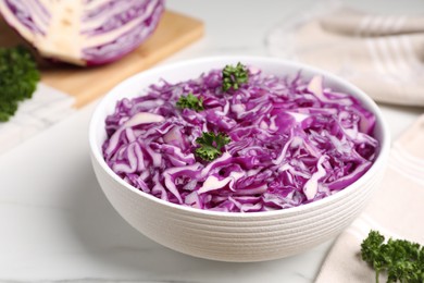 Photo of Bowl with shredded red cabbage and parsley on white table, closeup