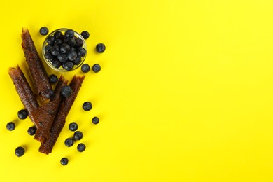 Delicious fruit leather rolls and blueberries on yellow background, flat lay. Space for text