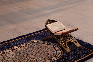 Rehal with open Quran and Muslim prayer beads on rug indoors. Space for text