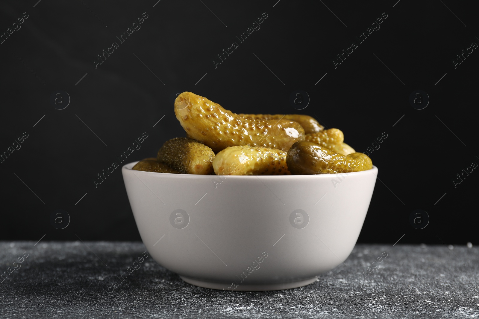 Photo of Tasty pickled cucumbers in bowl on grey textured table, closeup