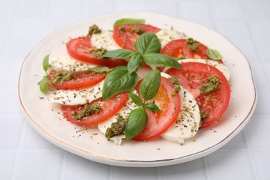 Photo of Plate of delicious Caprese salad with pesto sauce on white tiled table, closeup