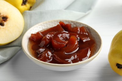 Tasty homemade quince jam in bowl and fruits on white wooden table, closeup