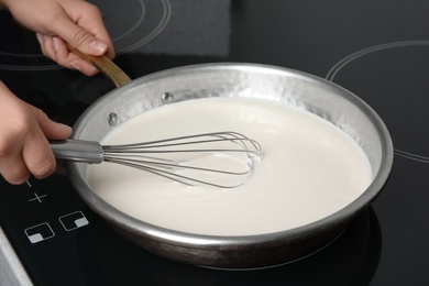 Photo of Woman cooking delicious creamy sauce in pan on stove, closeup