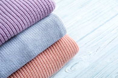 Photo of Stack of warm knitted clothes on wooden background, closeup