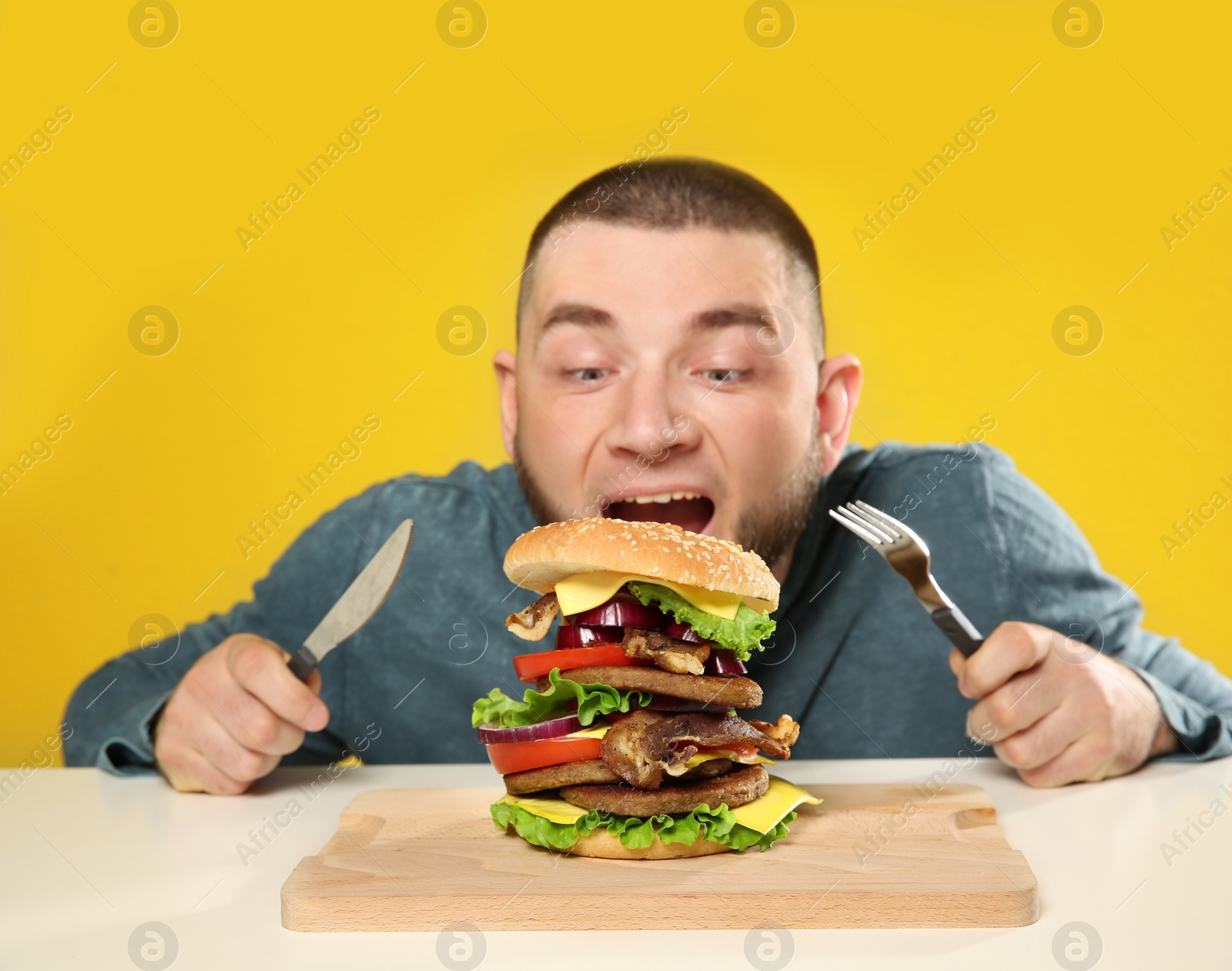 Photo of Young man with cutlery and tasty huge burger at table