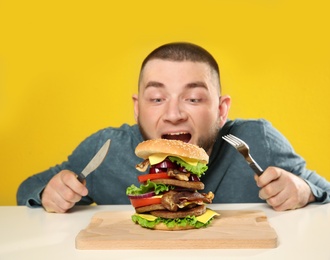 Young man with cutlery and tasty huge burger at table