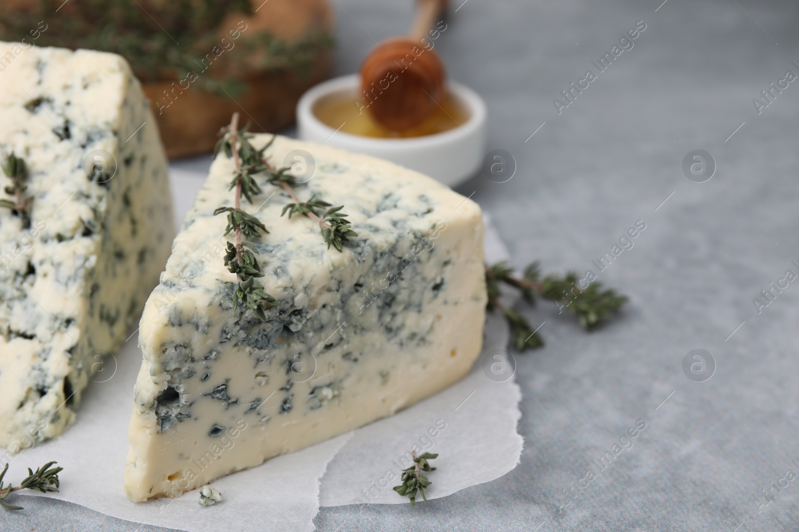 Photo of Tasty blue cheese with thyme on grey table, closeup. Space for text