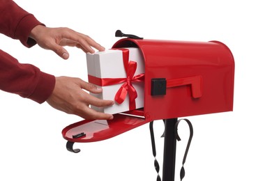 Man putting Christmas gift into mailbox on white background, closeup. Sending present by mail