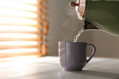 Photo of Pouring hot water into cup on white wooden table, space for text. Good morning