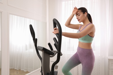 Tired woman after training on modern elliptical machine at home