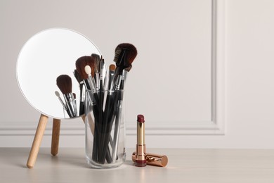 Photo of Set of professional brushes, lipstick and mirror on wooden table indoors, space for text