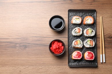 Delicious sushi rolls, soy sauce, ginger and chopsticks on wooden table, flat lay. Space for text