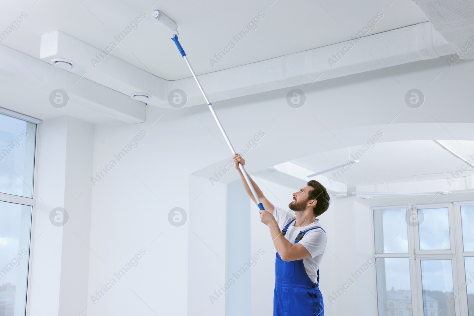 Photo of Handyman with roller painting ceiling in room