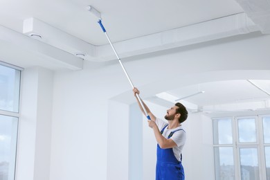 Photo of Handyman with roller painting ceiling in room