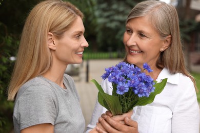 Photo of Happy daughter giving beautiful cornflowers to her mature mother outdoors