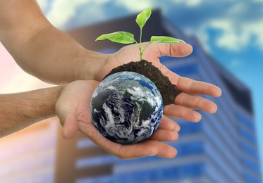 Image of Make Earth green. Man holding globe and soil with seedling against blurred building, closeup